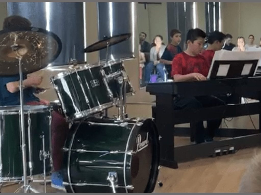 Kids engaging in a musical performance at CanCare Daycare, showcasing creativity and teamwork. Children performing on drums and piano in a school band recital at Cancare Daycare