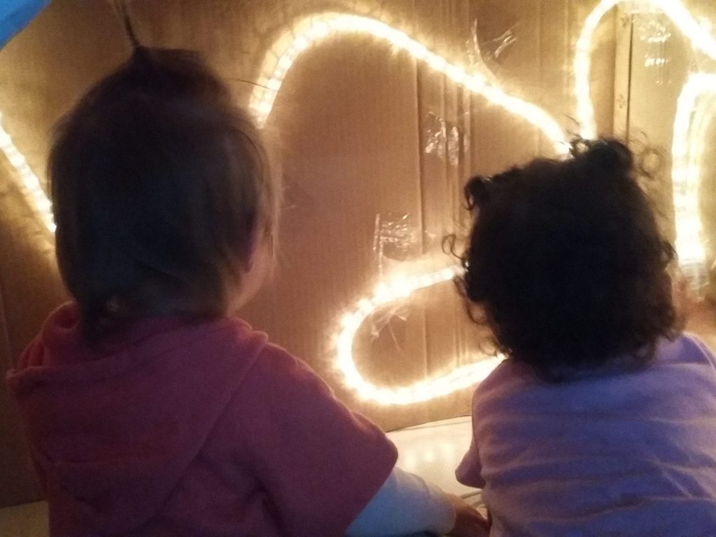 Kids engaged with glowing light art display at Cancare Daycare center. Two children observing illuminated light art installation at daycare.