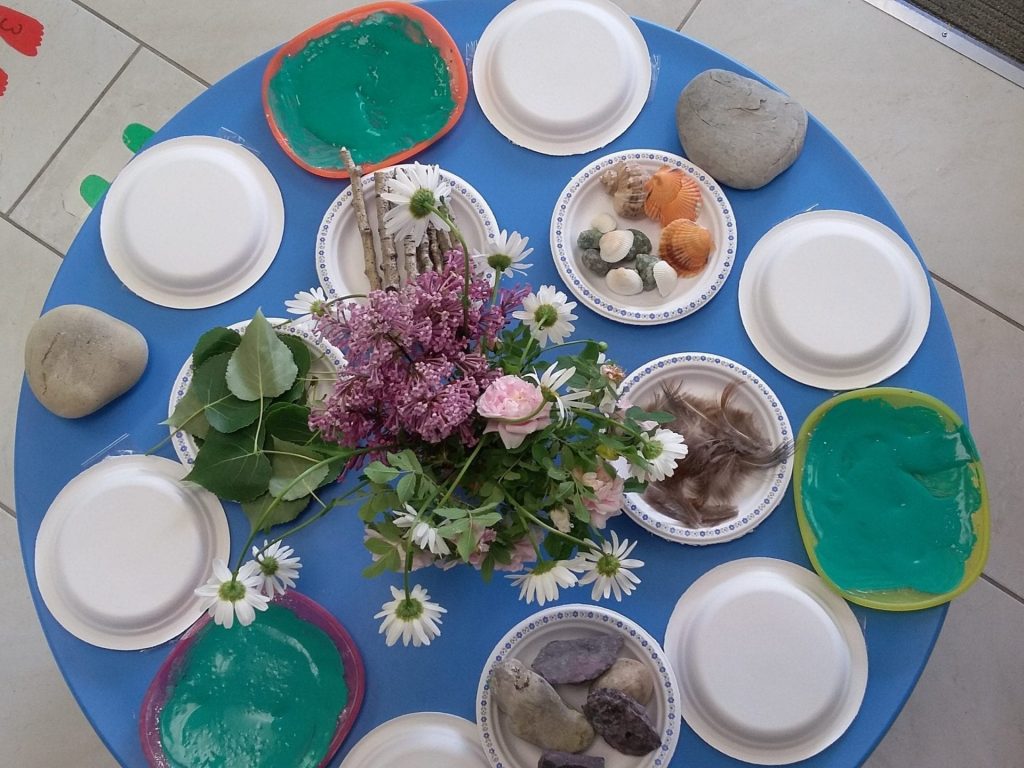 Colorful table setup with stones, flowers, and soap bars for children's activity at Cancare Daycare. Table setting with stones, flowers, and colorful soap bars for kids' activity.