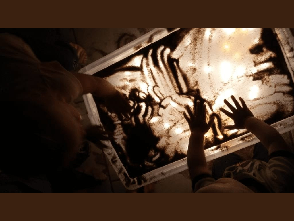 Kids engaging in creative sand art activity at Cancare Daycare, fostering imagination and fine motor skills. Children creating sand art on a lightbox at Cancare Daycare