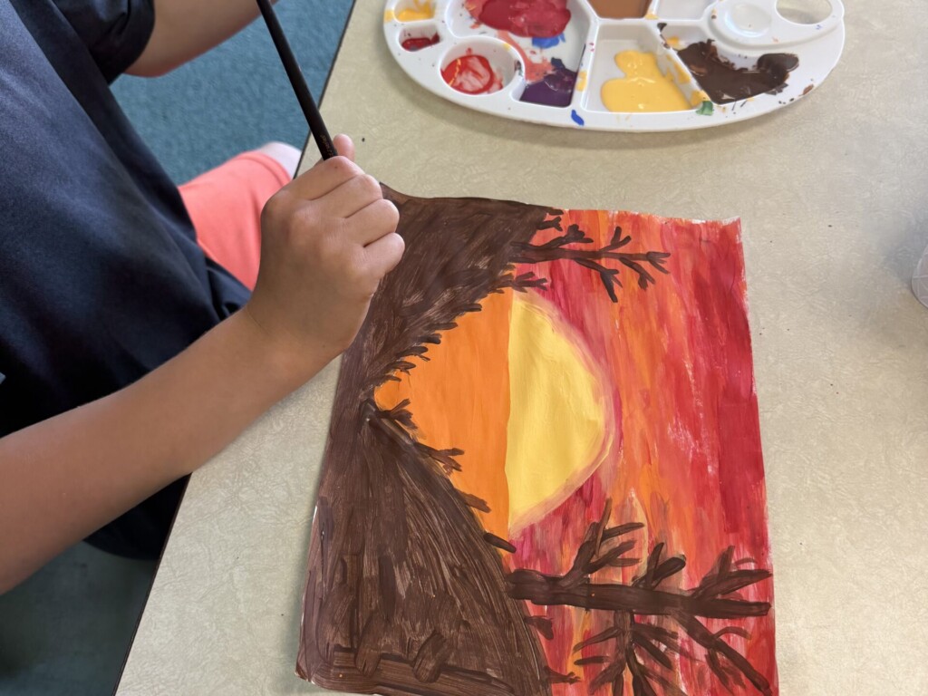 Child painting a sunset and tree silhouette scene