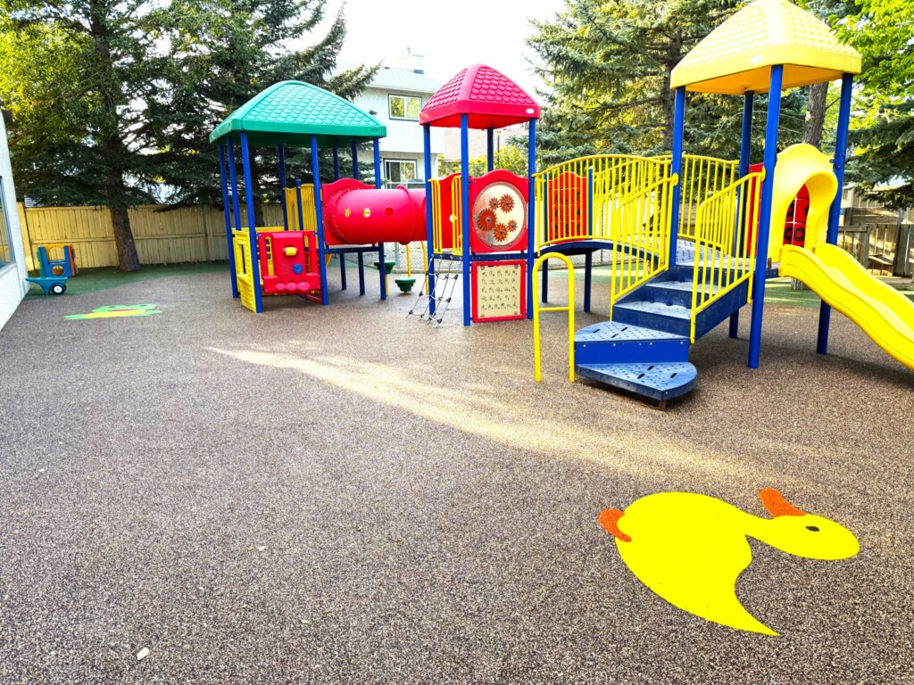 Colorful playground structure with slide and turtle floor decal, surrounded by trees