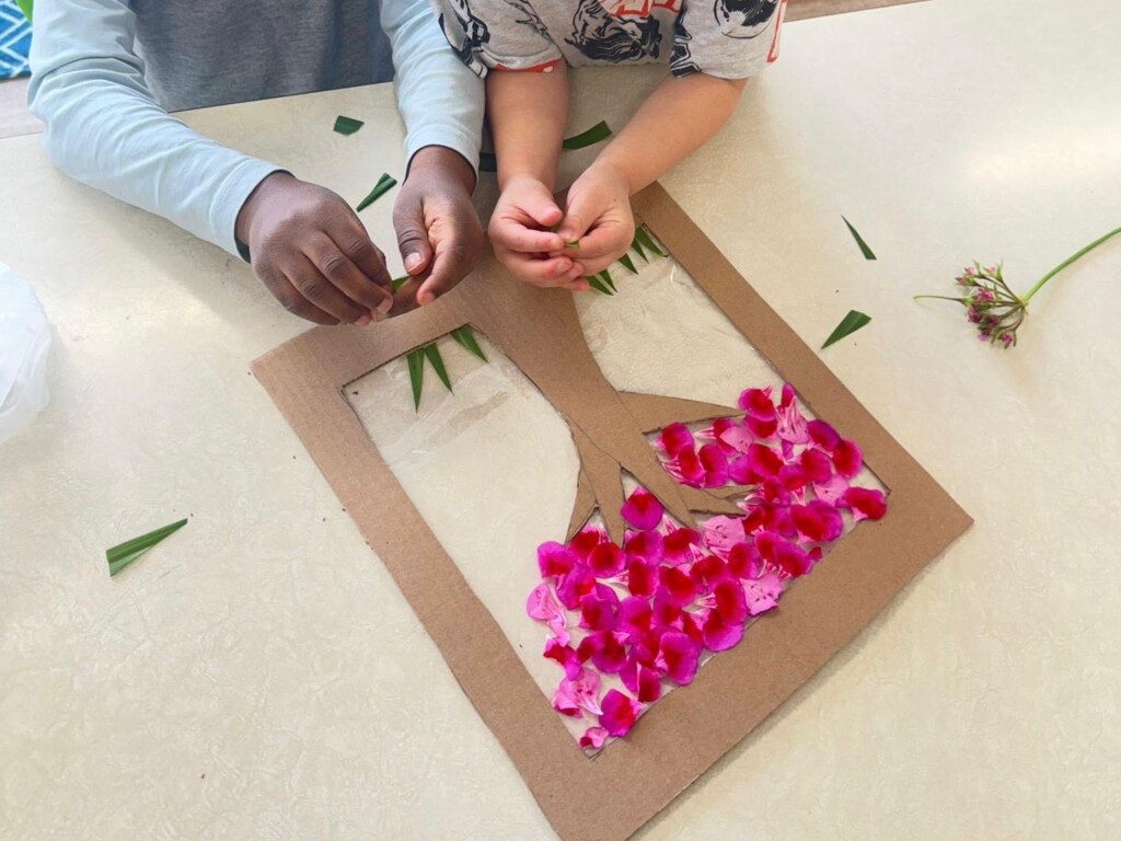 Children creating a pressed flower and leaf art project on a cardboard tree cutout