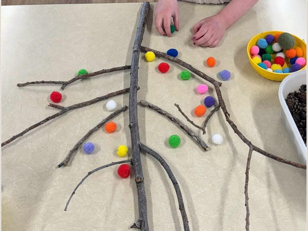 Colorful pom-poms placed on tree branches as a fine motor craft activity